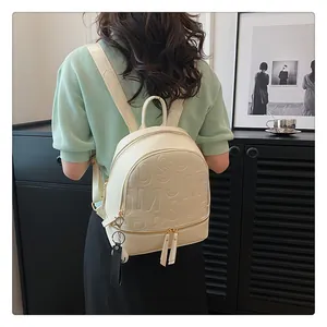 Detail of white PU leather backpack with letter embossing and golden metal hardware on a model