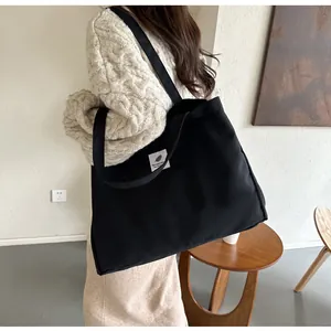 Détail d'un grand sac cabas en toile noire porté par un mannequin dans un intérieur