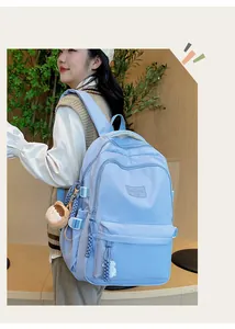 Detail showing a light blue nylon backpack with a plush bear pendant and brand logo patch