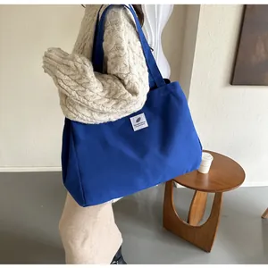 Grand sac cabas en toile bleu avec écusson blanc porté à l'épaule sur tenue beige