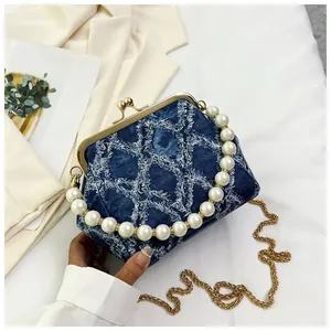 Detail of denim shell bag featuring pearl handle and gold clasp closure with chain