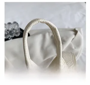 Close-up of the thick rounded handle and premium pebble-grain texture on a cream backpack