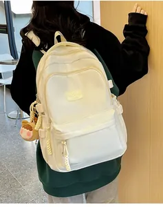 Detail of cream white nylon backpack with a cute cartoon charm and multiple zip pockets
