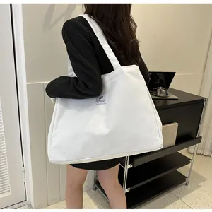 Détail d'un grand sac cabas en toile blanche avec un écusson plume au style minimaliste