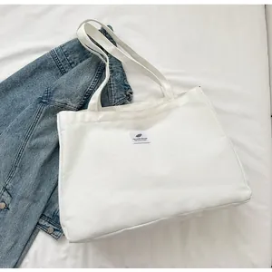 Détail d'un sac cabas en toile blanche avec broderie posé à côté d'une veste en jean