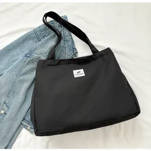 Détail d'un sac cabas en toile noire avec écusson blanc et anses de transport solides