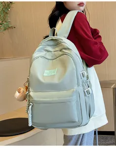Close-up of mint green nylon backpack with white buckles and brown bear plush charm