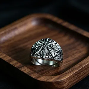 Close-up of vintage metal ring with embossed marijuana leaf pattern on a walnut tray