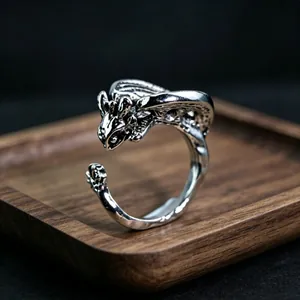 Macro detail of a silver dragon wrap ring featuring intricate scales and wings on wood