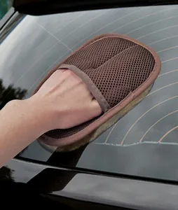 Macro view of a brown imitation wool car wash mitt cleaning a glass vehicle rear window