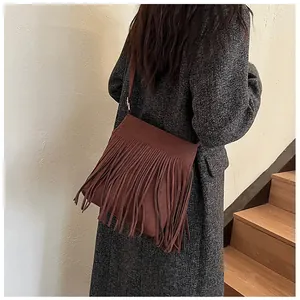 Détail d'un sac seau en daim marron foncé avec de longues franges sur un manteau en tweed