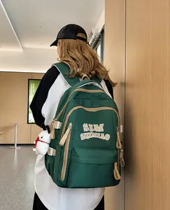 Forest green nylon backpack with white lettering and cute plush toy charm on model
