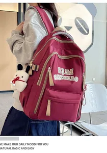 Detail of burgundy nylon backpack with multi-layer zippers and cute dog plush pendant
