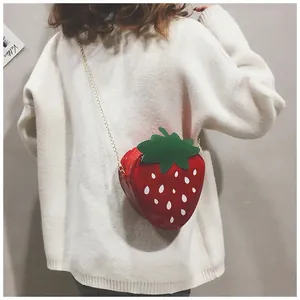 Détail du sac bandoulière fraise créatif avec chaîne dorée sur un pull blanc