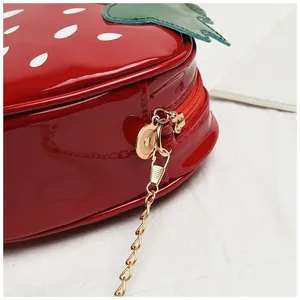 Gros plan du sac fraise en cuir verni avec fermeture éclair rouge et chaîne dorée