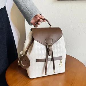 Quilted beige bucket backpack with brown leather trim and smiley face charm on wood table