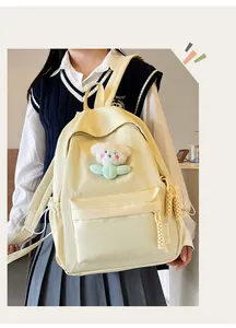 Détail d'un sac à dos en nylon jaune crème avec un petit ours en peluche et des breloques