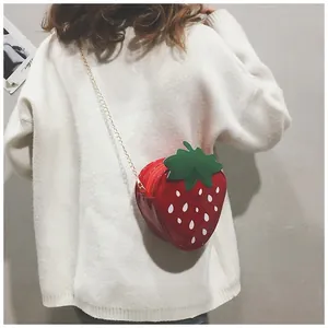 Sac à bandoulière chic en forme de fraise rouge avec chaîne dorée porté par un mannequin