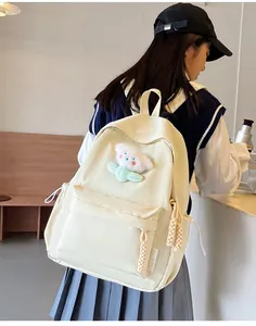 Vue détaillée d'un sac à dos en toile blanc crème avec un joli charme de fleur en peluche