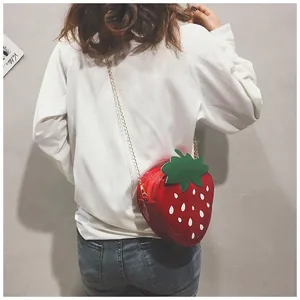 Détail d'un sac bandoulière fraise 3D avec une chaîne dorée porté par un mannequin