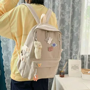 Detalle de mochila crema con insignias de dibujos animados y colgante de osito de peluche