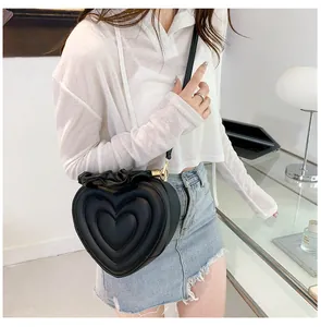Detailed view of heart-shaped black crossbody bag with ruffles on model with casual outfit