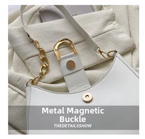 Detailed close-up of white crescent bag featuring a premium golden metal magnetic buckle