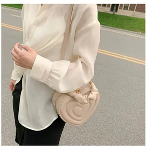 Detalle del bolso beige en forma de corazón con asa fruncida y cremallera dorada metal
