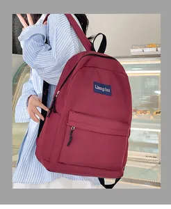 Detail eines weinroten Nylon-Rucksacks mit Markenaufnäher und Vordertasche im Innenraum