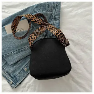 Detail view of black canvas crossbody bag with geometric pattern woven wide strap