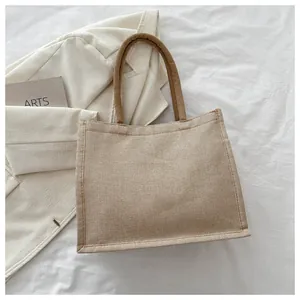 Détail d'un sac cabas en jute avec poignées tissées sur une surface en tissu blanc épuré