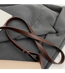 Dettaglio della tracolla lunga in pelle marrone su una borsa a tracolla color crema