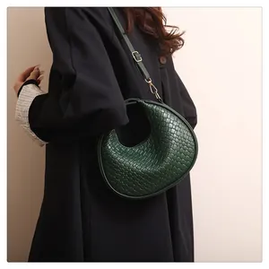 Detail of dark green woven leather handbag featuring a unique hollow half-moon handle design