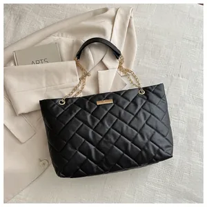 Detail of black quilted tote bag featuring golden chain straps and metallic buckle