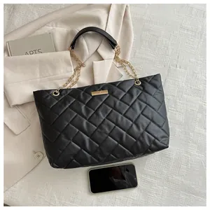 Detail of black quilted tote bag with gold chain strap and size comparison to smartphone