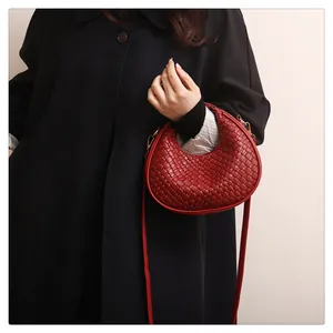 Detail of burgundy woven crossbody bag with diamond lattice texture and golden hardware