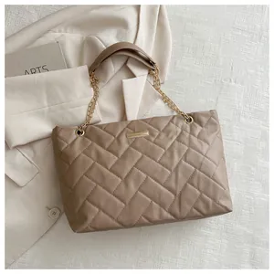 Detail of quilted tote bag with diamond pattern, gold chain strap and metal nameplate