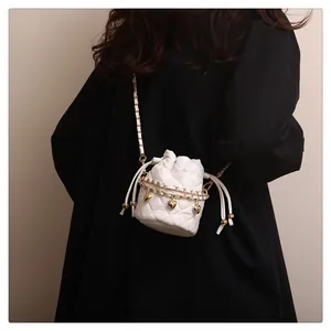 Detail einer weißen gesteppten Mini-Beuteltasche mit goldenen Herzanhängern und Kettengurt