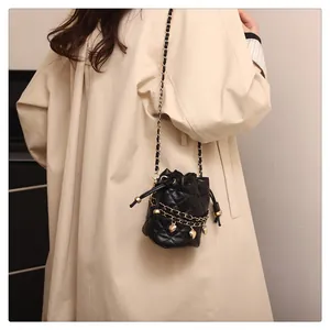 Detail der Mini-Stepp-Beuteltasche in Schwarz mit Goldkette und Herzanhänger am Trenchcoat