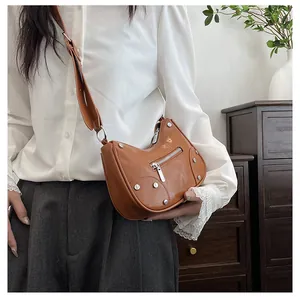 Close-up of caramel leather dumpling bag showing silver rivets and metallic zipper detail