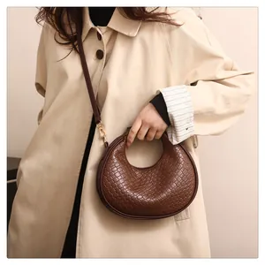 Close-up of brown woven half-moon crossbody bag styled with a beige trench coat on a model