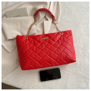 Detail of red quilted tote bag with large diamond stitching and gold chain strap