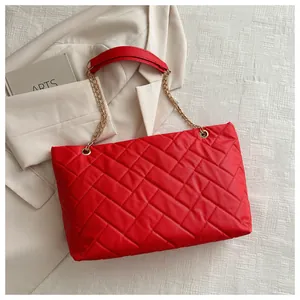 Detailed macro view of quilted red faux leather surface and golden chain strap of the tote bag