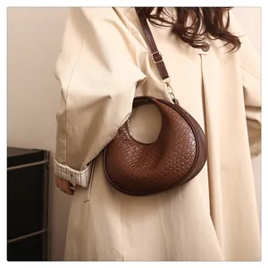 Détail du sac demi-lune marron à texture tressée avec boucles métalliques dorées
