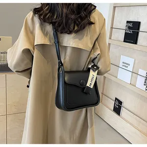 Dettaglio di una borsa a tracolla retrò nera con cinturino logo e stile trench beige