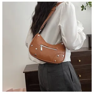 Close-up of brown crescent moon bag with silver studs worn with casual white shirt