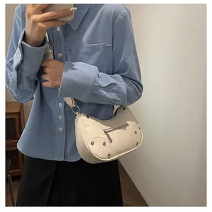 Detail of cream croissant bag with silver studs on model showing shoulder wear style