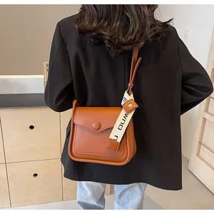 Dettaglio della borsa a tracolla in pelle marrone con nastro decorativo e fibbia rotonda