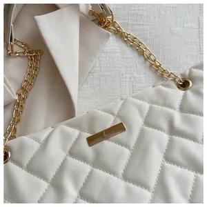 Close-up of white quilted tote bag featuring a gold chain strap and rectangular metal logo