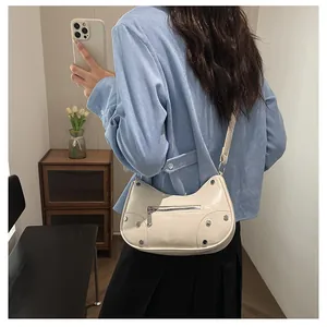 Detail view of cream dumpling bag with silver rivets worn as a trendy shoulder bag